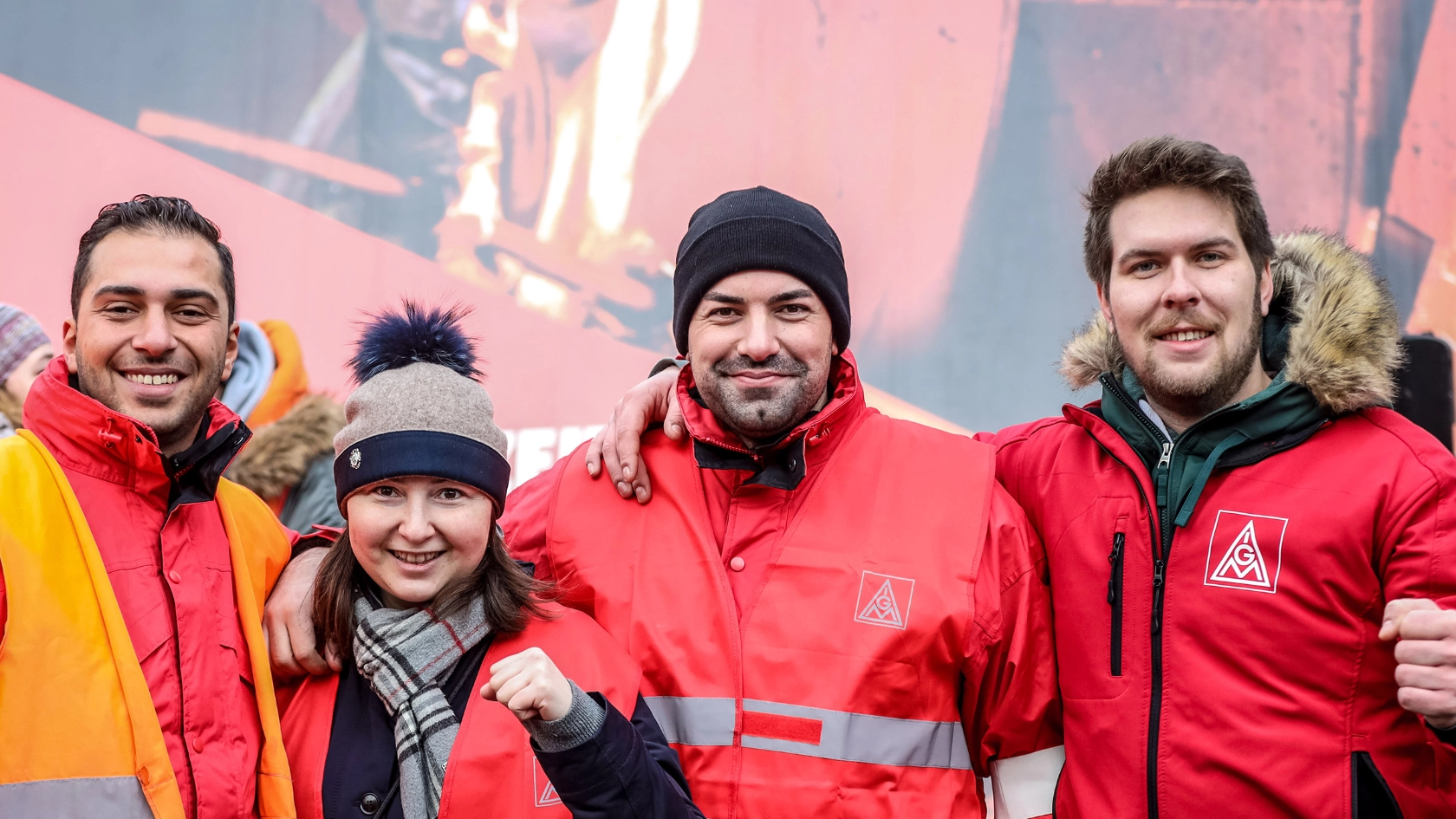 Eine Frau und drei Männer ballen die Fäuste und lächeln in die Kamera.